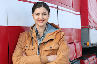 Camionera de pie junto a un camión con una sonrisa porque tiene protección de boletos CDL, descuentos en tarjetas de combustible y acceso a abogados CDL de TVC Pro-Driver