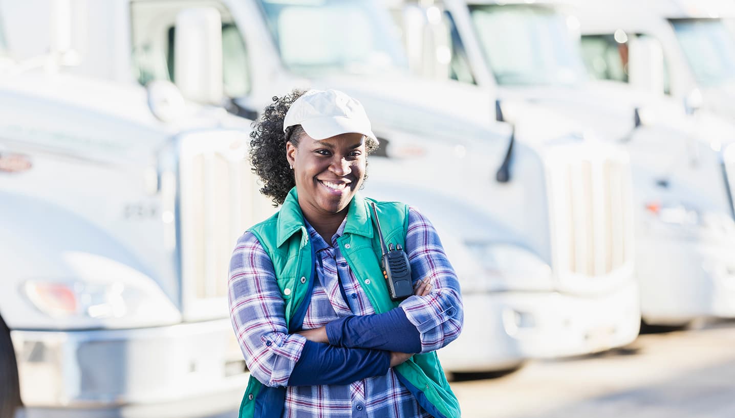 Female truck driver with TVC Pro-Driver CDL ticket protection smiling with trucks in background