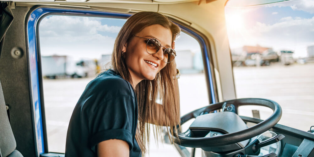 Portrait of young woman professional truck driver sitting and driving big truck. Inside of vehicle. People and transportation concept.