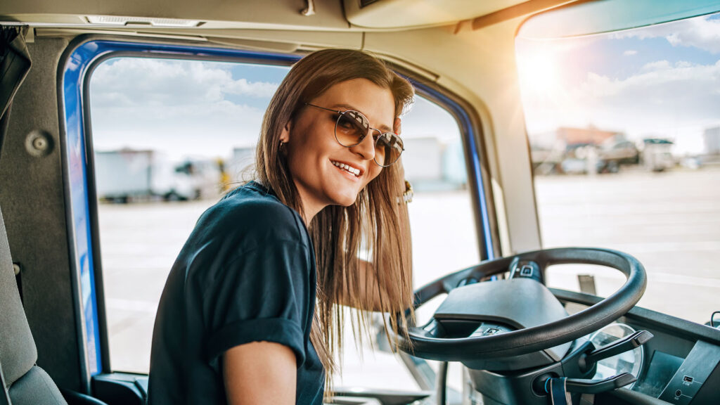 Portrait of young woman professional truck driver sitting and driving big truck. Inside of vehicle. People and transportation concept.
